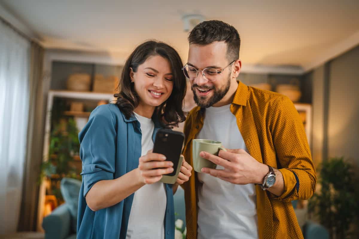 happy couple smiling and looking at their phone in their house